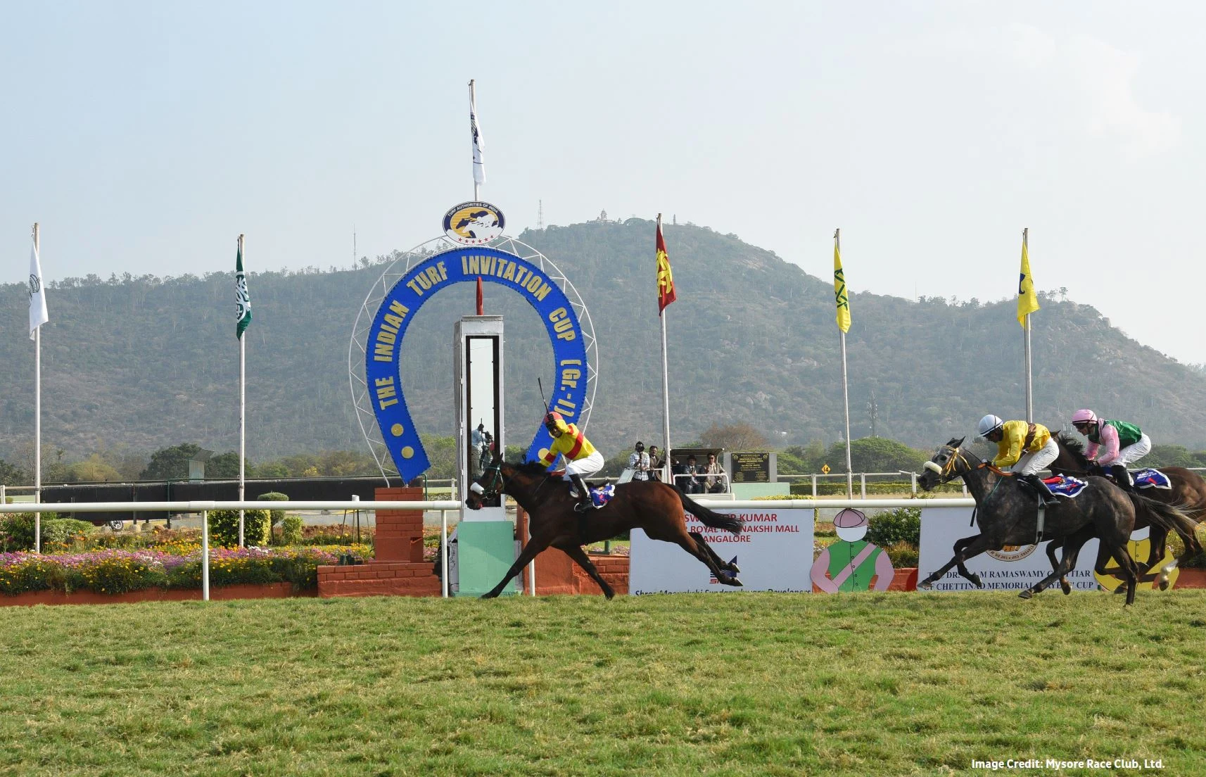 Racehorses passing the Indian Turf Invitation Cup winning post at Mysore with hills behind