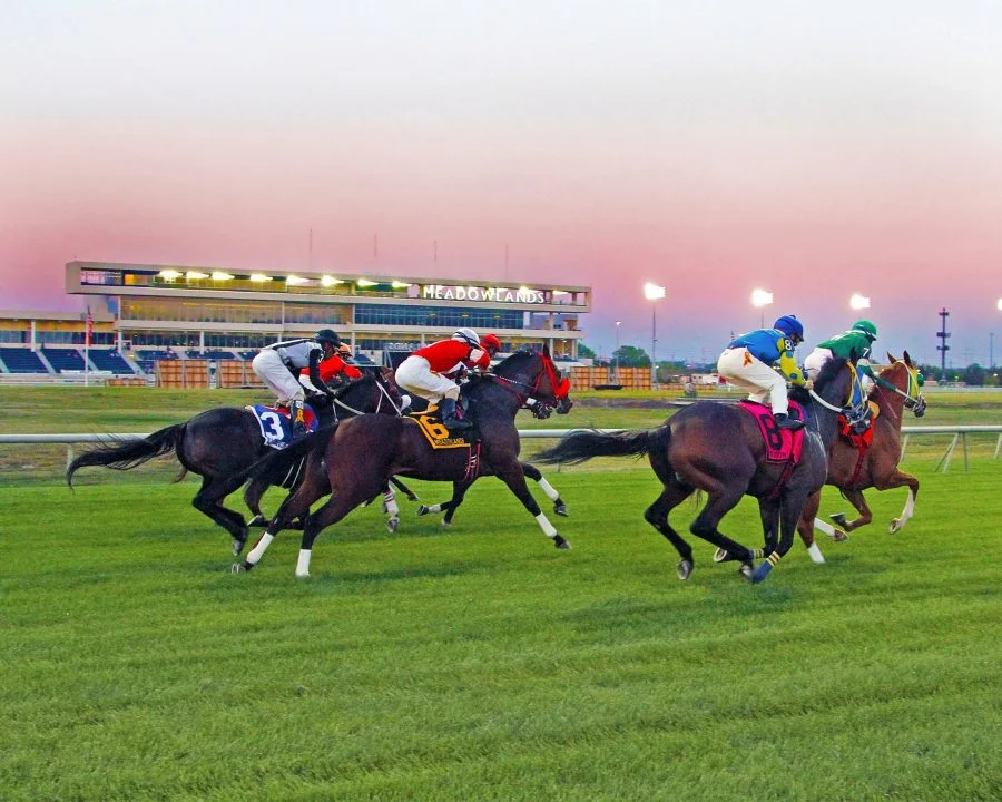 Mounted racehorses on turf in front of the Meadowlands grandstand