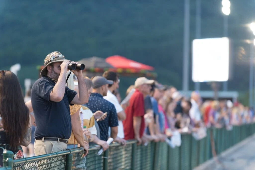 Racegoers watching from the rail at Penn National, including a fan using binoculars