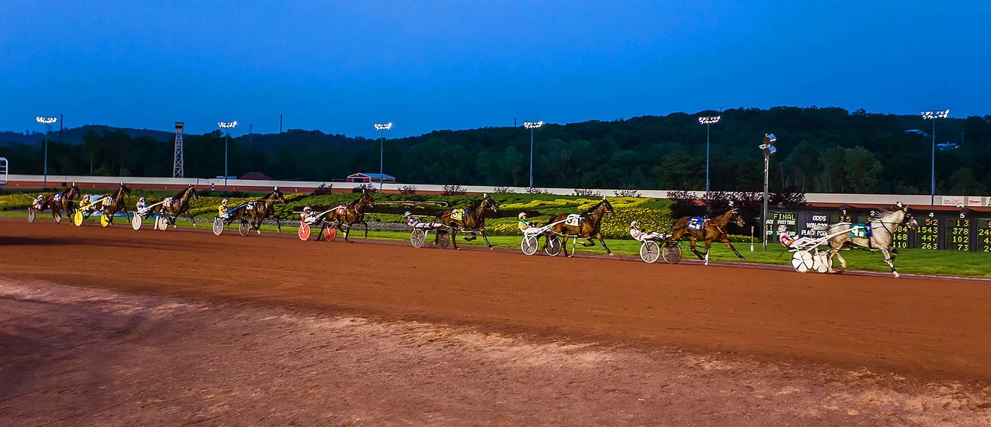 Harness horses race along Pocono Downs with the infield and tote board behind them